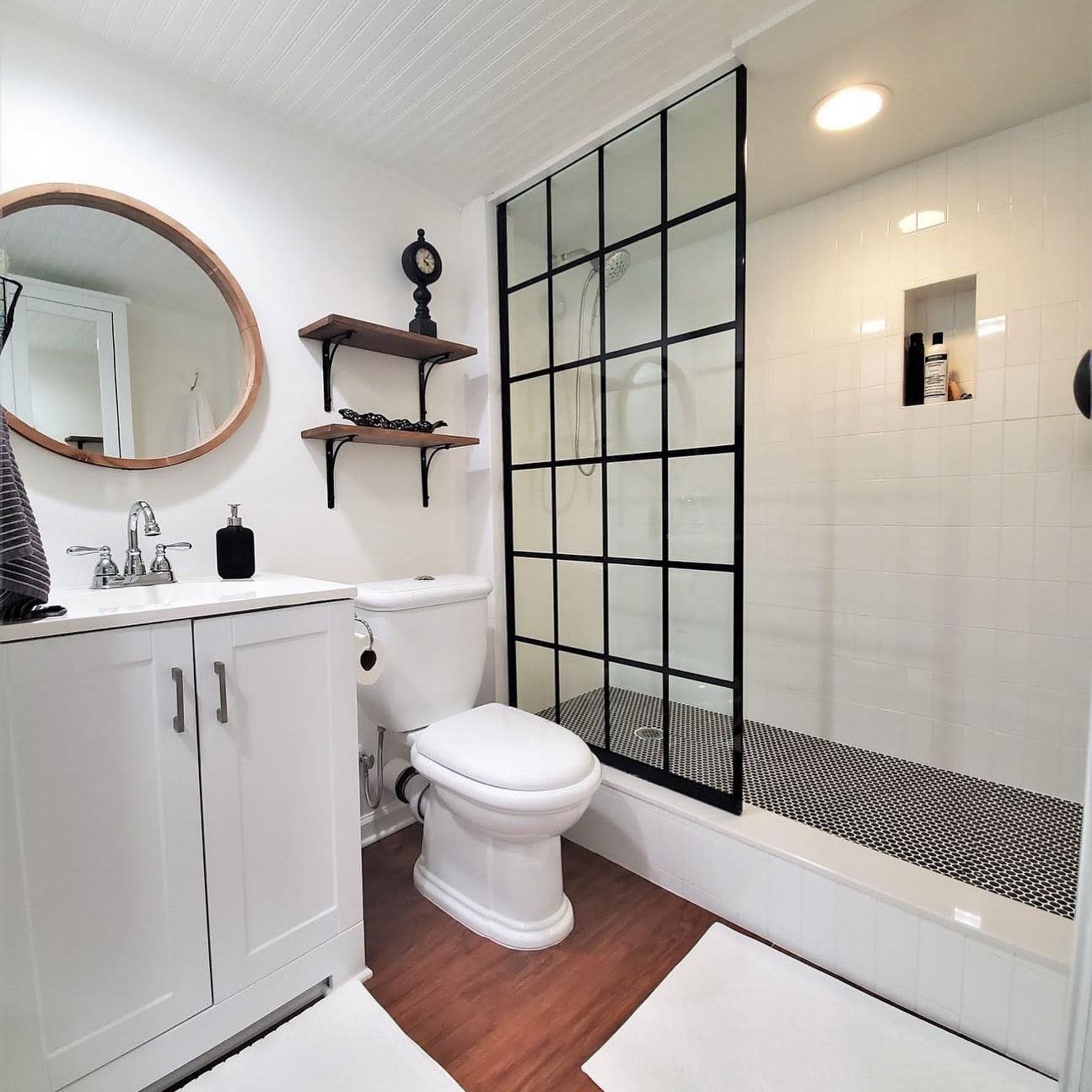 Modern bathroom with black grid glass shower, white vanity, and round mirror.
